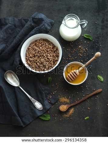 Rustic healthy breakfast set. Cooked buckwheat groats with milk and honey on dark grunge backdrop. Top view
