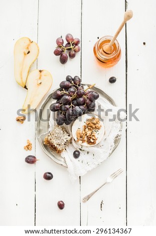 Camembert cheese with grape, walnuts, pear and honey on vintage metal plate over white rustic wood backdrop, top view