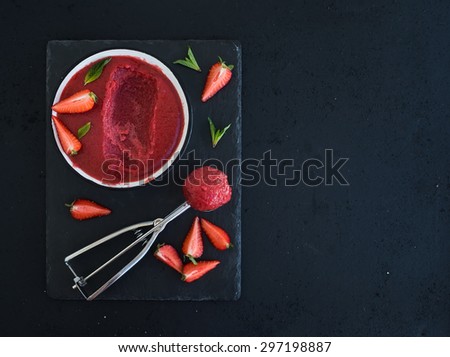 Strawberry sorbet or ice-cream with fresh berries, mint and metal scooper on black slate tray over dark grunge backdrop, top view, copy space