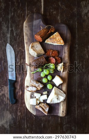 Wine appetizers set: meat and cheese selection, grapes and bread on a rustic wooden board over a dark wood background. Top view, copy space