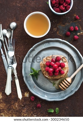 Breakfast set. Buckwheat pancakes with fresh raspberries, honey and mint leaves over grunge metal background, top view, selective focus