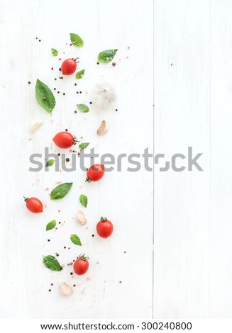 Cherry tomatoes, fresh basil leaves, garlic cloves and spices on rustic white wooden backdrop, top view, copy space