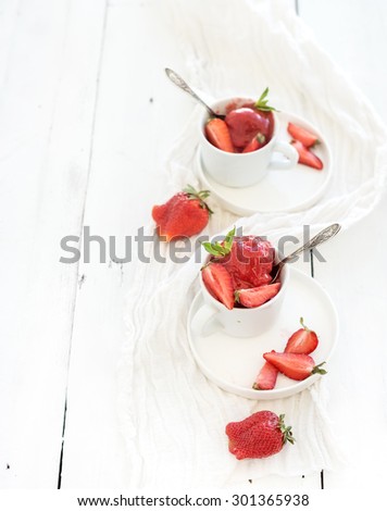 Strawberry sorbet ice-cream with mint leaves in cups over rustic white wooden background, top view, copy space