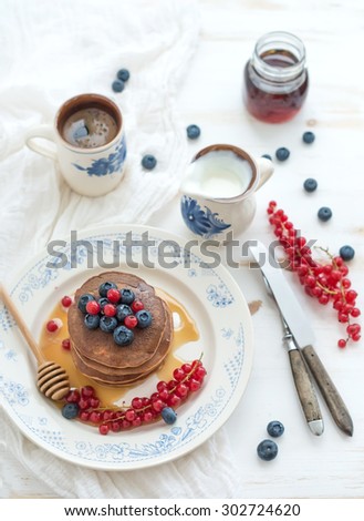 Breakfast set. Buckwheat pancakes with fresh berries, honey, sour cream and cup of coffee over white wooden background, top view