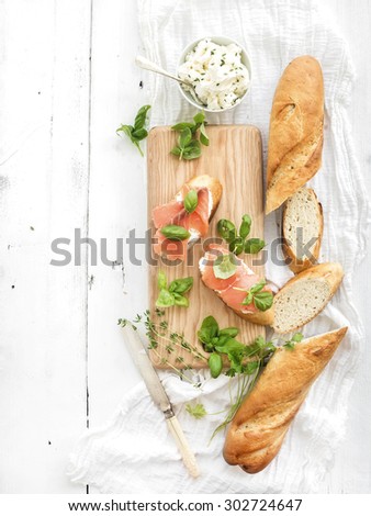 Salmon, ricotta and basil sandwiches with baguette on a rustic wooden board over white wood background. Top view, copy space