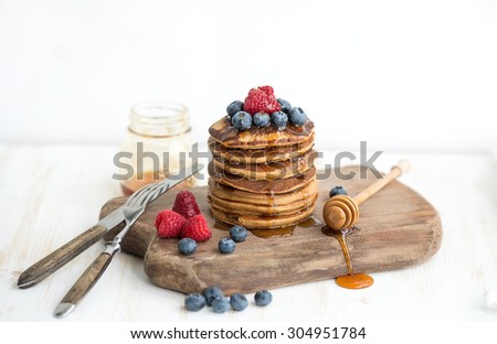 Buckwheat pancakes with fresh berries and honey on rustic wooden board, white backdrop