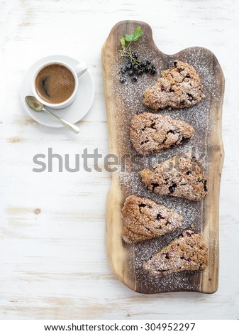 Fresh blackcurrant scones with cup of coffee over rustic walnut wood serving board, top view, copy space