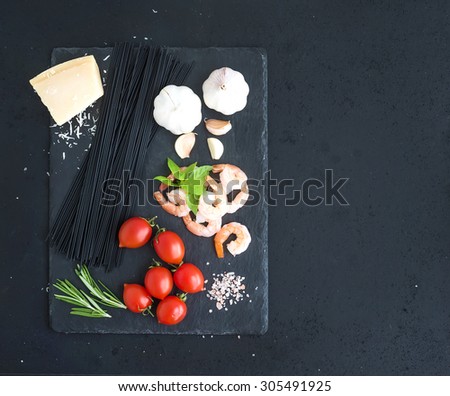 Ingredients for black pasta with seafood. Shrimps, spaghetti, basil, garlic, spices, parmesan cheese and  cherry-tomatoes on dark grunge backdrop, top view, copy space