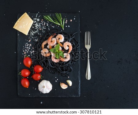 Black pasta spaghetti with shrimps, basil, pesto sauce, garlic, Parmesan cheese and cherry-tomatoes on a slate tray over black grunge backdrop, top view, copy space