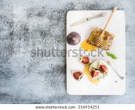 Camembert or brie cheese with fresh figs, honeycomb and glass of white wine on white serving board over grunge rustic grey backdrop, top view, copy space