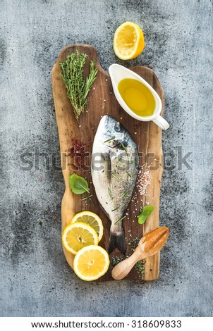 Fresh uncooked dorado or sea bream fish with lemon, herbs, oil and spices on rustic wooden board over grunge backdrop, top view