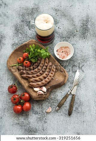 Grilled sausages with vegetables on rustic serving board and mug of light beer over grunge  backdrop