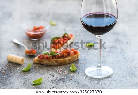 Wine appetizer set. Glass of red wine, brushettas with fresh tomato and basil on over rustic grunge grey backdrop