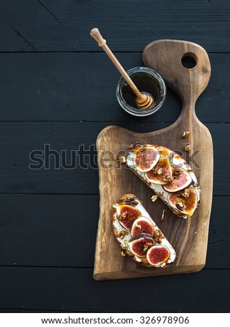 Sandwiches with ricotta, fresh figs, walnuts and honey on rustic wooden board over black backdrop, top view