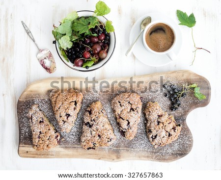 Fresh blackcurrant scones with coffee and bowl of berries over rustic walnut wood serving board, top view, copy space
