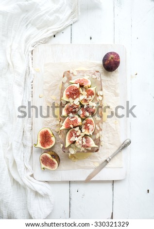 Loaf cake with figs, almond and white chocolate on wooden serving board over white background, top view