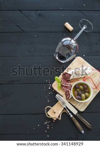 Wine appetizer set. Glass of red wine, French sausage and olives on black wooden backdrop, top view, copy space