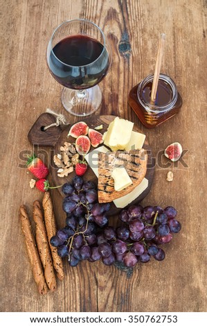 Glass of red wine, cheese board, grapes,fig, strawberries, honey and bread sticks  on rustic wooden table, top view