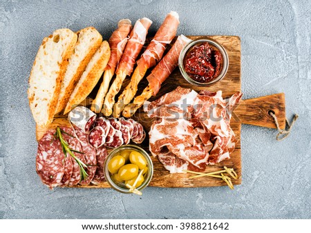 Meat appetizer selection or wine snack set. Variety of smoked meat, salami, prosciutto, bread sticks, baguette, olives and sun-dried tomatoes on rustic wooden board, top view, horizontal