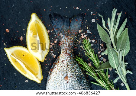 Tail of fresh raw Dorado or sea bream fish on black slate stone board with spices, herbs, lemon and salt. Top view