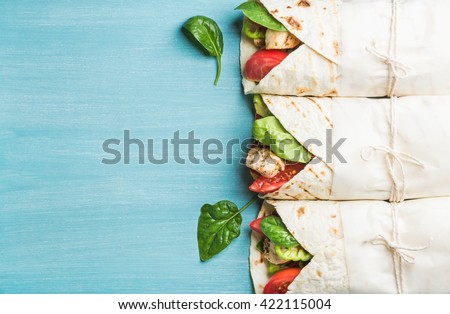 Healthy lunch snack. Tortilla wraps with grilled chicken fillet and fresh vegetables on blue painted wooden background. Top view, copy space