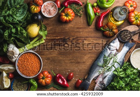 Ingredients for cooking healthy dinner. Raw uncooked seabass fish with vegetables, grains, herbs and spices over rustic wooden background. Copy space, top view