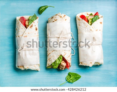 Healthy lunch snack. Tortilla wraps with grilled chicken fillet and fresh vegetables on blue painted wooden background. Top view