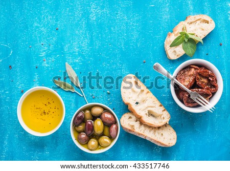Mediterranean snacks set. Olives, oil, sun-dried tomatoes, herbs and sliced ciabatta bread on over blue painted background, top view, copy space