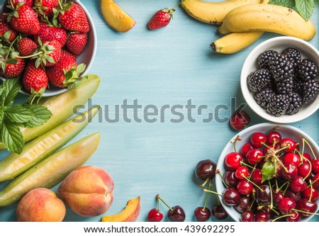 Healthy summer fruit variety. Sweet cherries, strawberries, blackberries, peaches, bananas, melon slices and mint leaves on blue backdrop with copy space in center, top view