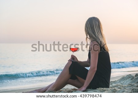 Young blond woman enjoying glass of rose wine on beach by the sea at sunset. Cleopatra beach, Alanya, Mediterranean region, Turkey.