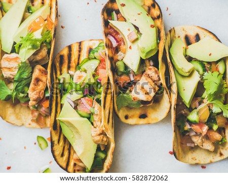 Healthy corn tortillas with grilled chicken fillet, avocado, fresh salsa, limes over light grey marble table background, top view. Healthy food, gluten-free, allergy-friendly, weight loss concept