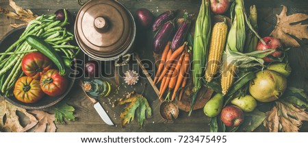 Fall healthy cooking background. Ingredients for Thanksgiving day dinner. Flat-lay of beans, corn corn, carrot, tomatoes, eggplants, fruits and fallen leaves over wooden table, top view