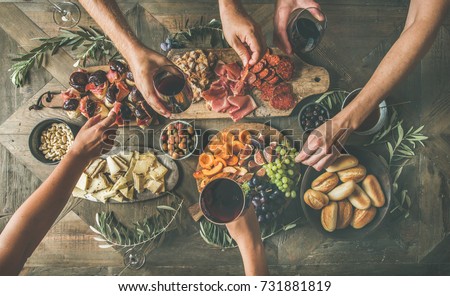 Flat-lay of friends eating and drinking together. Top view of people having party, gathering, celebrating at wooden rustic table set with various wine snacks and fingerfoods. Hands holding glasses