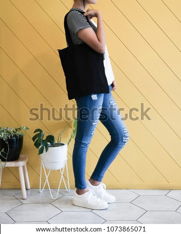 woman showing black totebag. Tote bag mock up for designer. In fun background, pink yellow and green pallete