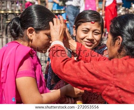 SWAYAMBHUNATH, KATHMANDU, NEPAL-OCTOBER 17, 2008: A woman puts Tika on young women\'s forehead to bless them with abundance during Dashain festival. Tika is a mixture of rice, yogurt and vermilion.
