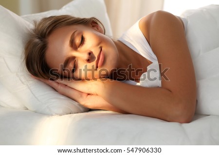 Beautiful young woman sleeping while lying in bed comfortably and blissfully. Sunbeam dawn  on her face