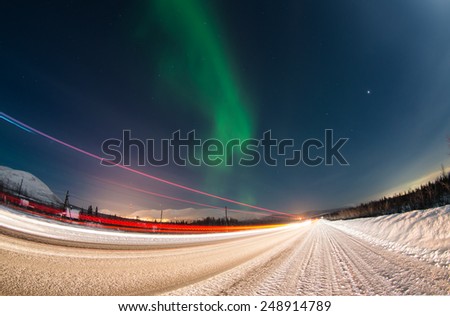 Northern lights over winter road with light trails from moving cars near Apatity town in Murmansk region (Kola peninsula) in northern Russia - long exposure nature background