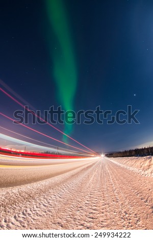 Northern lights over winter road with light trails from moving cars near Apatity and Kirovsk towns in Murmansk region (Kola peninsula) in northern Russia - long exposure nature background