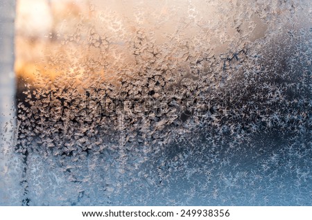 Sunset sky, view through the frozen window glass with hoarfrost drawings, taken in cold weather from inside of the building