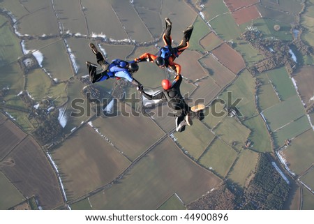 Three skydivers in free fall with snow in the background