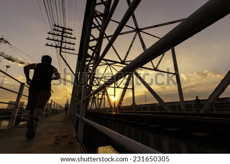 evening time view of a man running along situate old steel bridge structure and railway