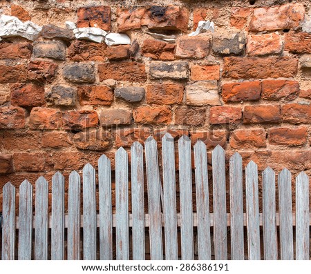The wall of different color ancient bricks and a wooden fence.