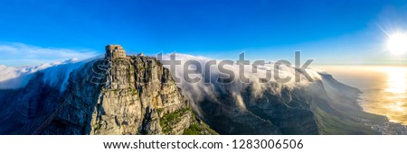 Table Mountain cable way covered in clouds sweeping over the twelve apostles during sunset in Cape Town