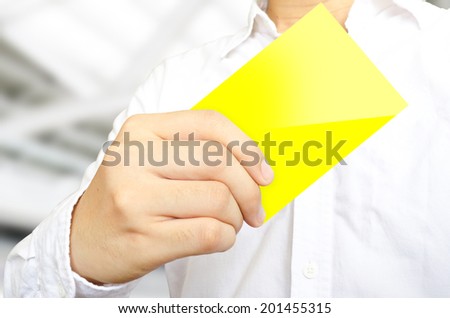 The business man in white shirt is showing the yellow card on blur office background.