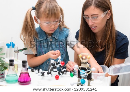 Science school, Workshop. A woman teacher and girl child collect molecules and conduct chemical experiments. On the table is a robot. STEM education.