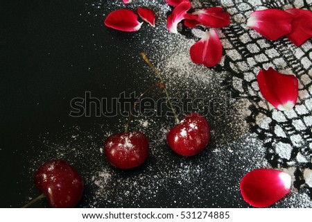 Sweet cherry against black background, lacy drawing from icing sugar and red rose petals