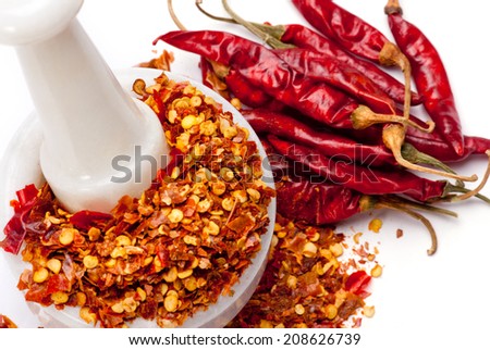 Red Chili Pepper Flakes in white granite pestle; mortar and scattered Red Chili Peppers; isolated on white background