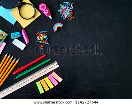 Back to school education supplies concept. Multicolored stationary office equipment on black blackboard background. Copy space. Place for text.