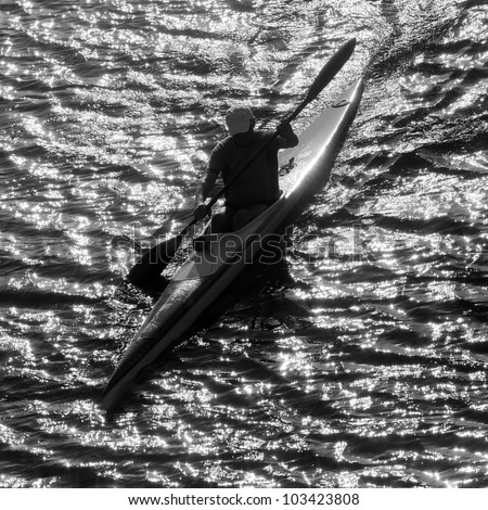 Silhouette of man kayaking in the lake at sunset. Classical black and white photography of high contrast scene.