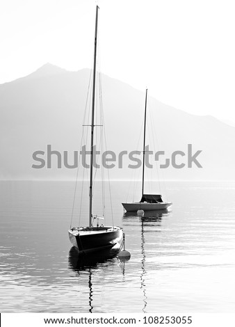 Two sail boats in early morning on the mountain lake. Black and white photography. Salzkammergut, Austria.